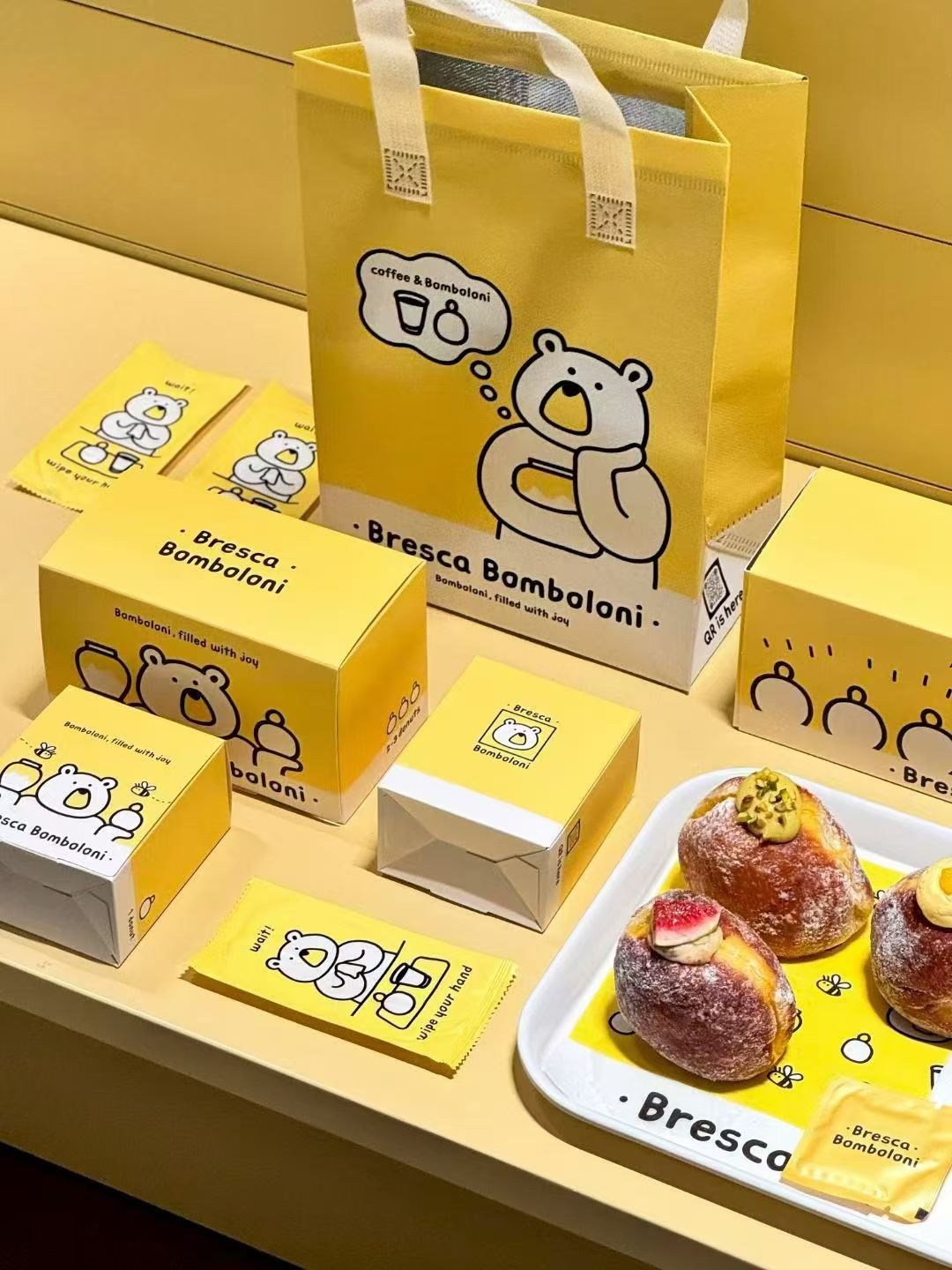 Bright yellow bakery packaging reference with pastry boxes, paper bag, wraps and serving tray.